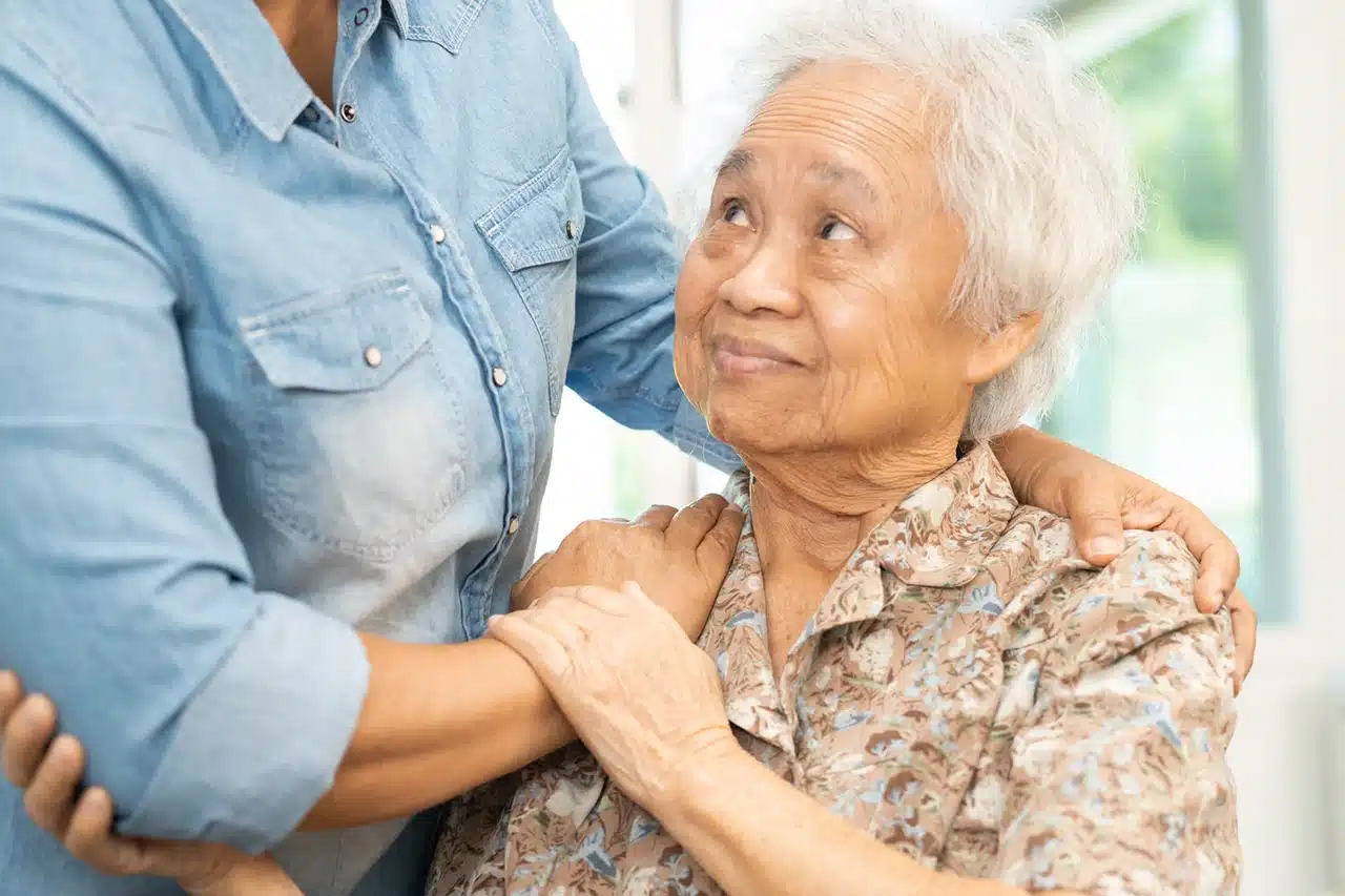 Aidant soutenant une femme âgée pour l'aider à se lever, illustration de la perte d'autonomie chez les personnes âgées