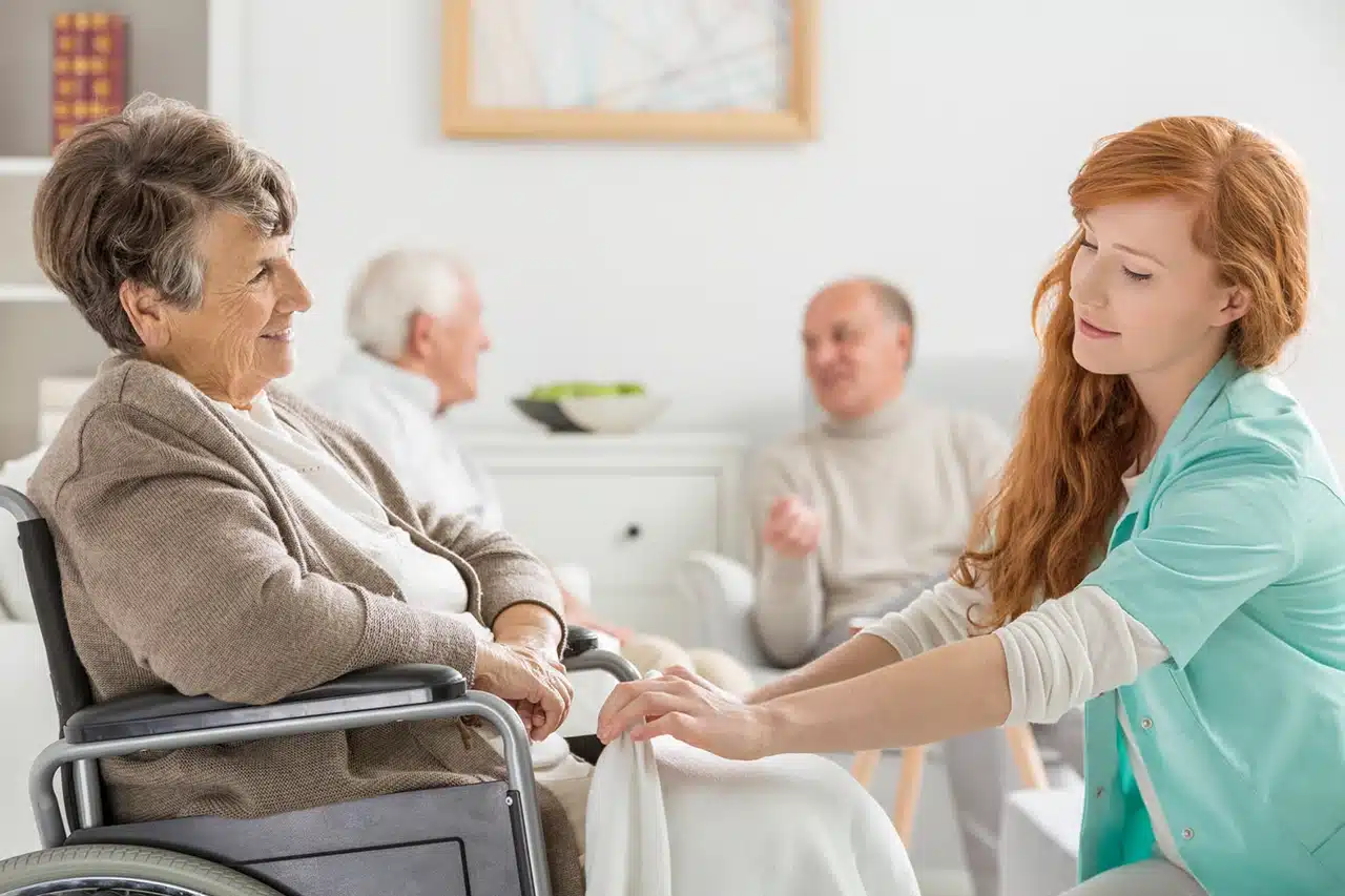 Aide-soignante accompagnant une personne âgée en fauteuil roulant dans une résidence