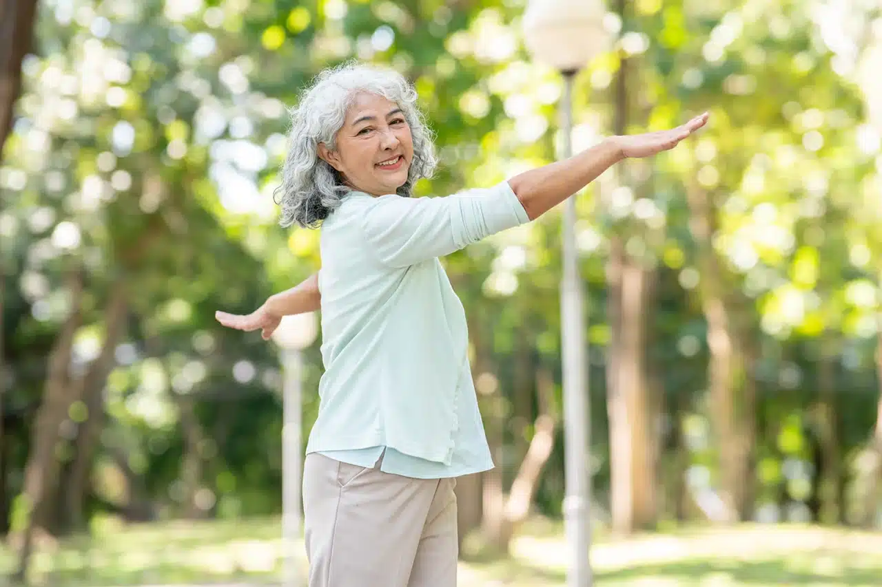 Smiling elderly woman doing stretching exercises in a park to maintain her health and balance