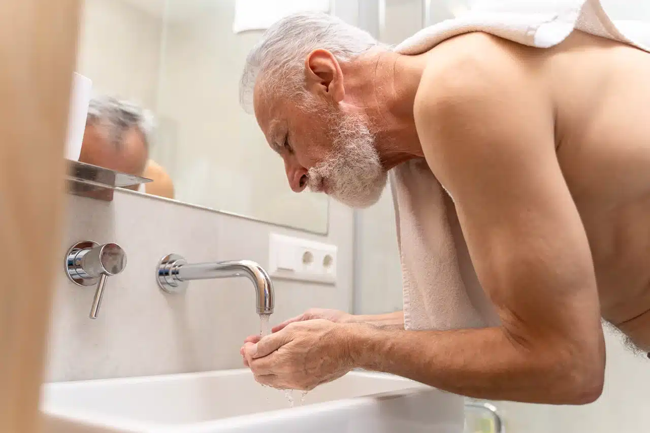 Elderly man washing his face at the sink in the bathroom during his daily hygiene routine