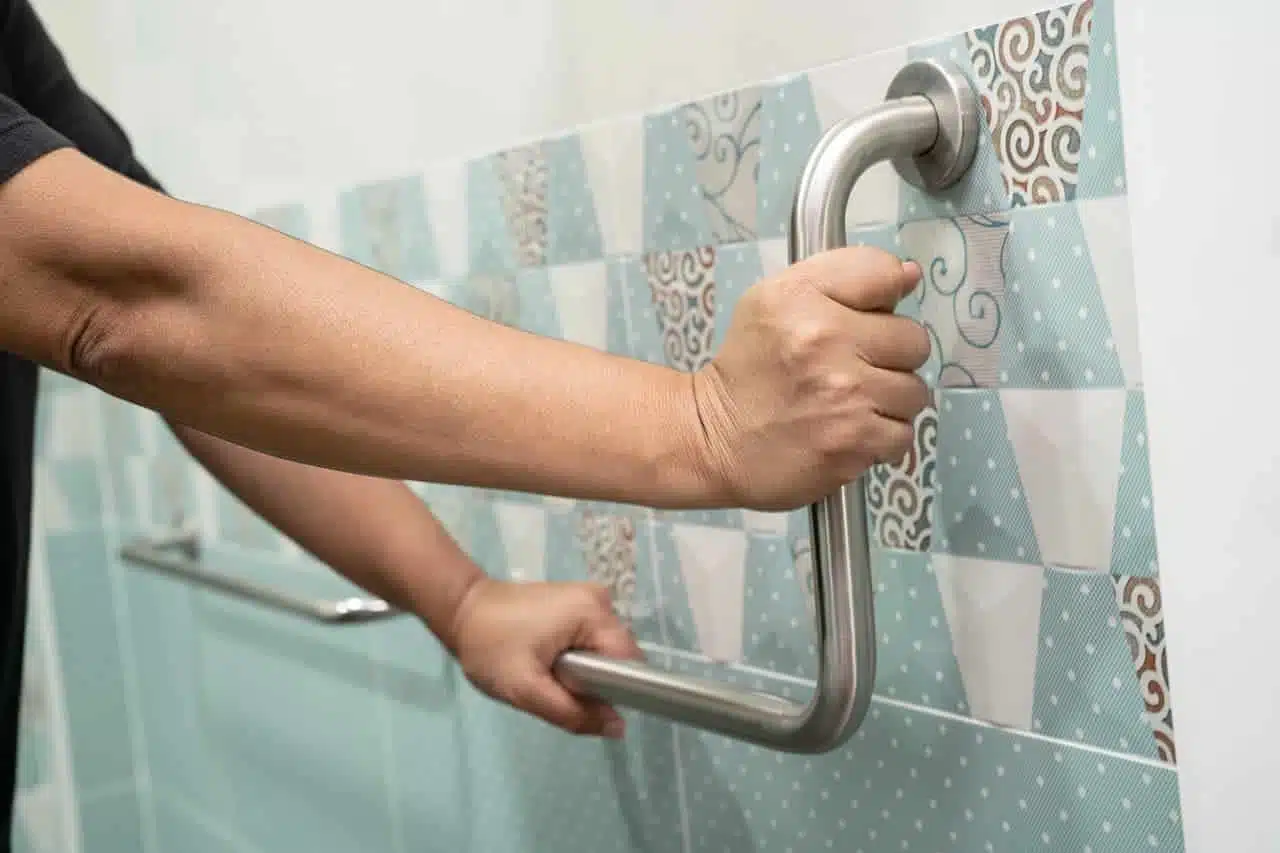 Hand gripping a wall-mounted grab bar in the bathroom to prevent falls in a person with Parkinson's disease