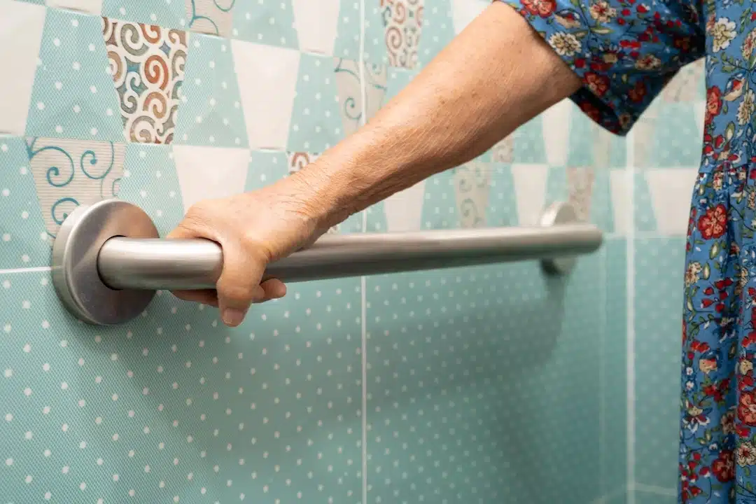 Older adult hand gripping a bathroom grab bar to improve stability and help prevent falls.
