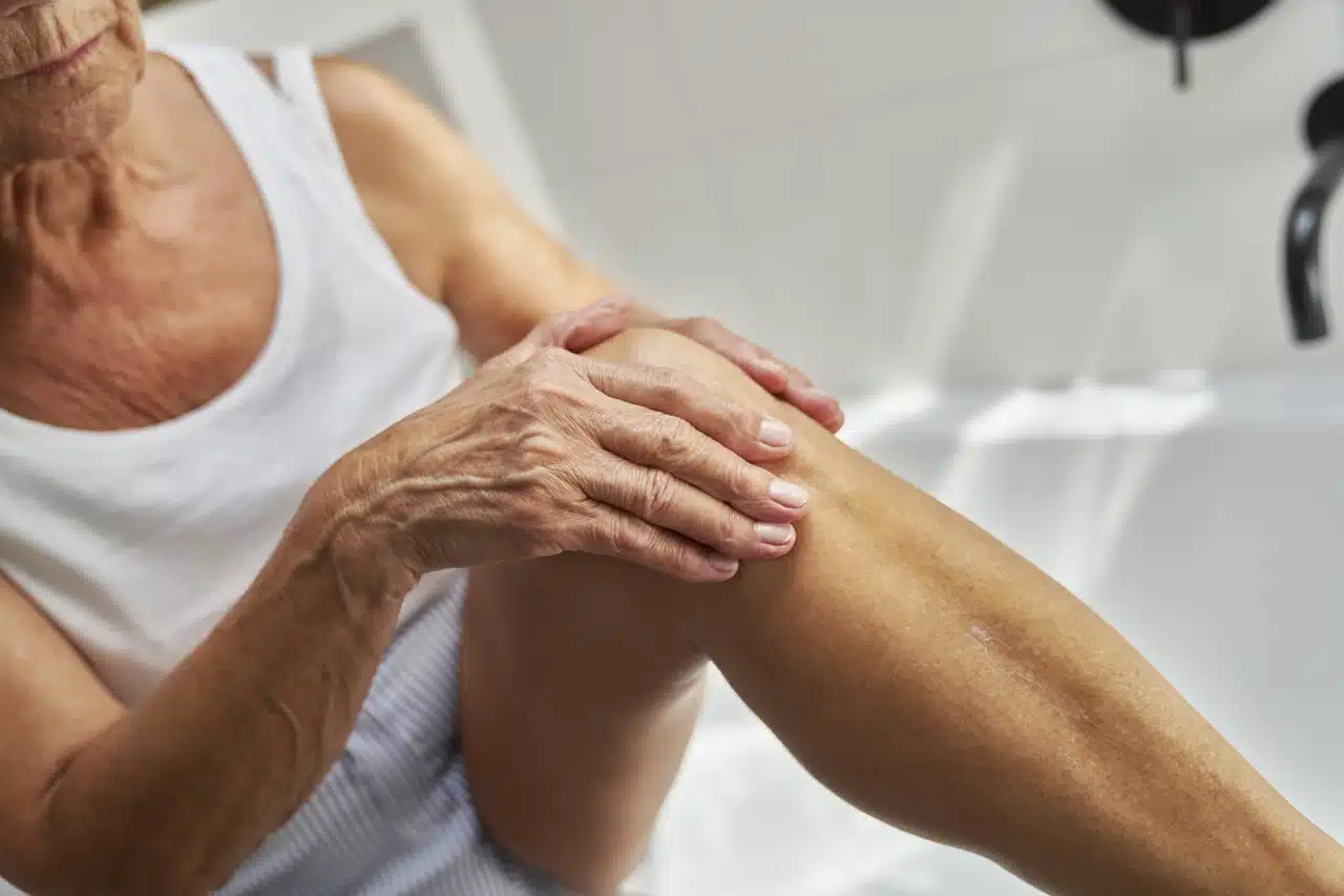 Personne âgée massant sa jambe dans la salle de bain pour soulager une douleur musculaire ou articulaire.