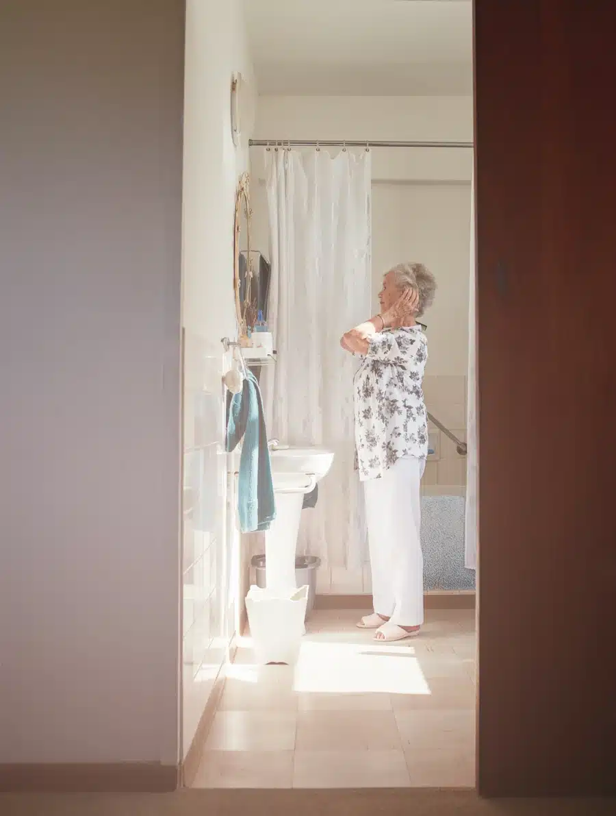 Older adult in a bathroom, illustrating an adapted environment with supportive equipment.