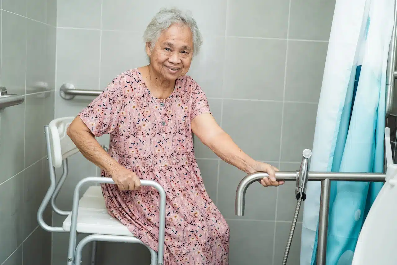 Smiling older adult on a bath seat with grab bars, symbolizing independence and safety.